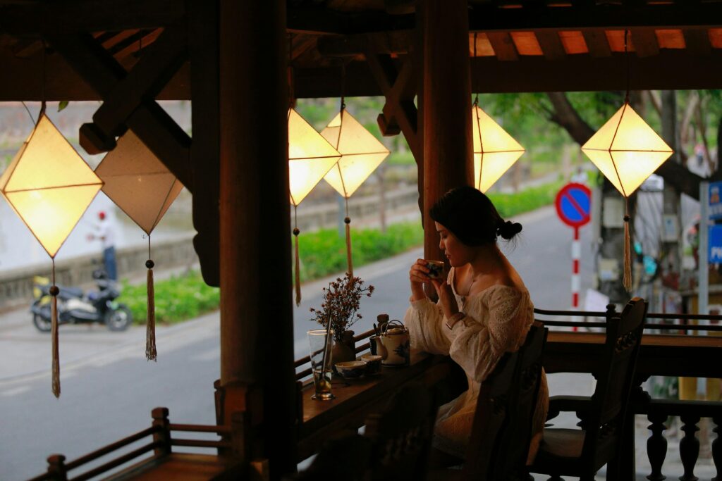 A woman relaxing with a cup of tea under warm lighting in an outdoor café setting.