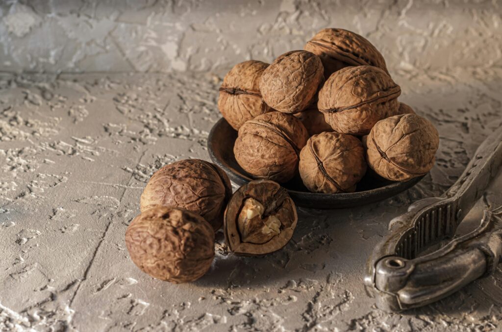 A rustic presentation of walnuts in a dish with a nutcracker on a textured background.