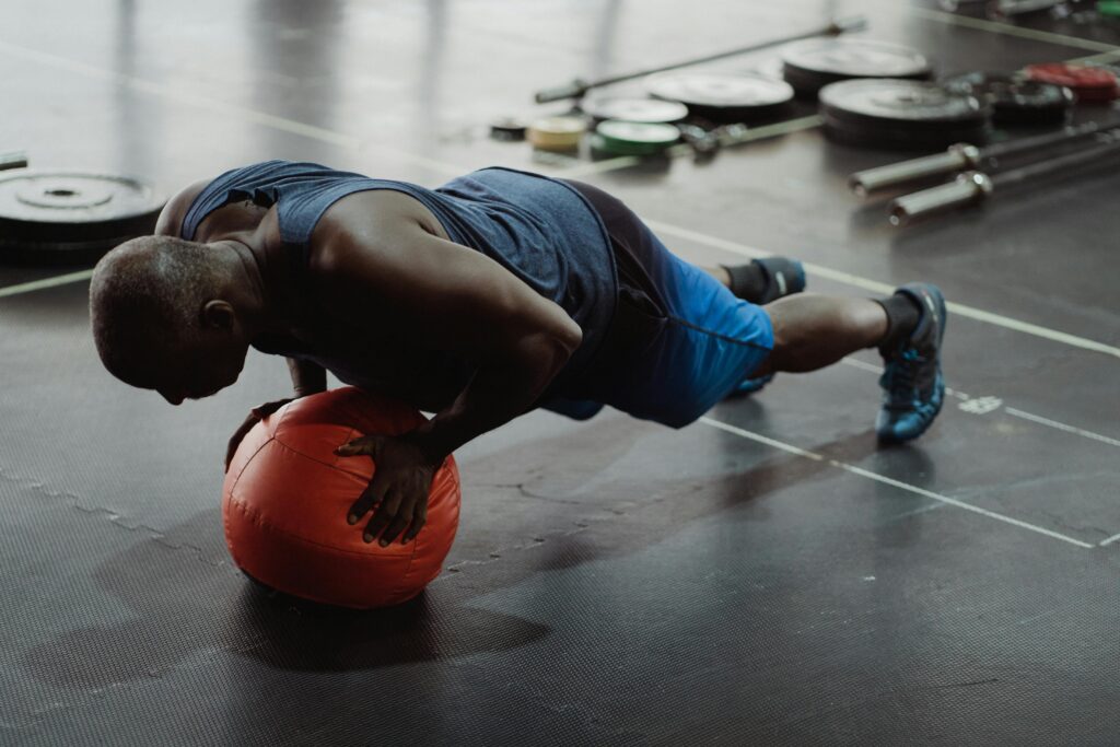 Adult man in gym doing push-up on a medicine ball, demonstrating strength and balance.