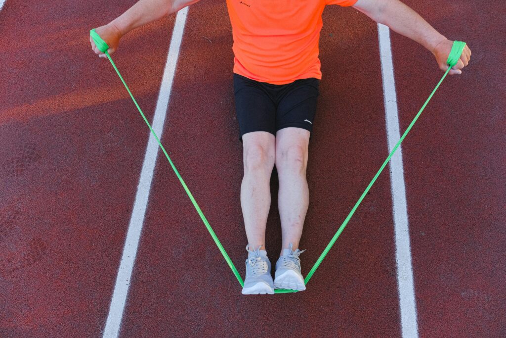 An adult male athlete working out with a green resistance band on a running track. Perfect for fitness and wellness themes.