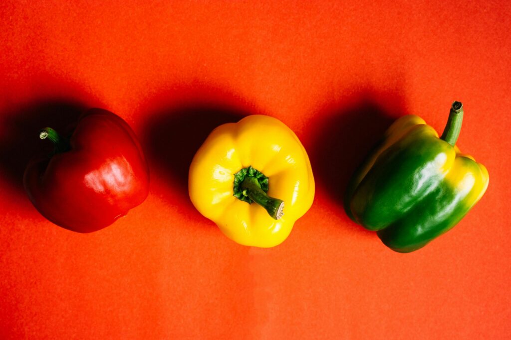 A colorful display of red, yellow, and green bell peppers on a vivid red background.