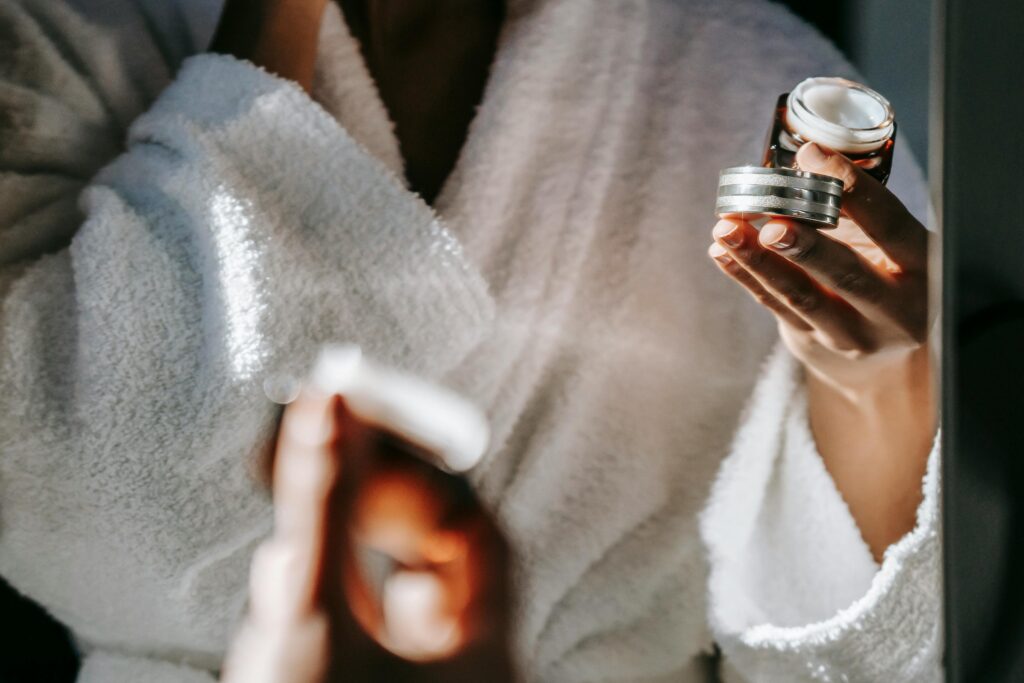 Woman in bathrobe applying skincare cream for a calm morning routine.