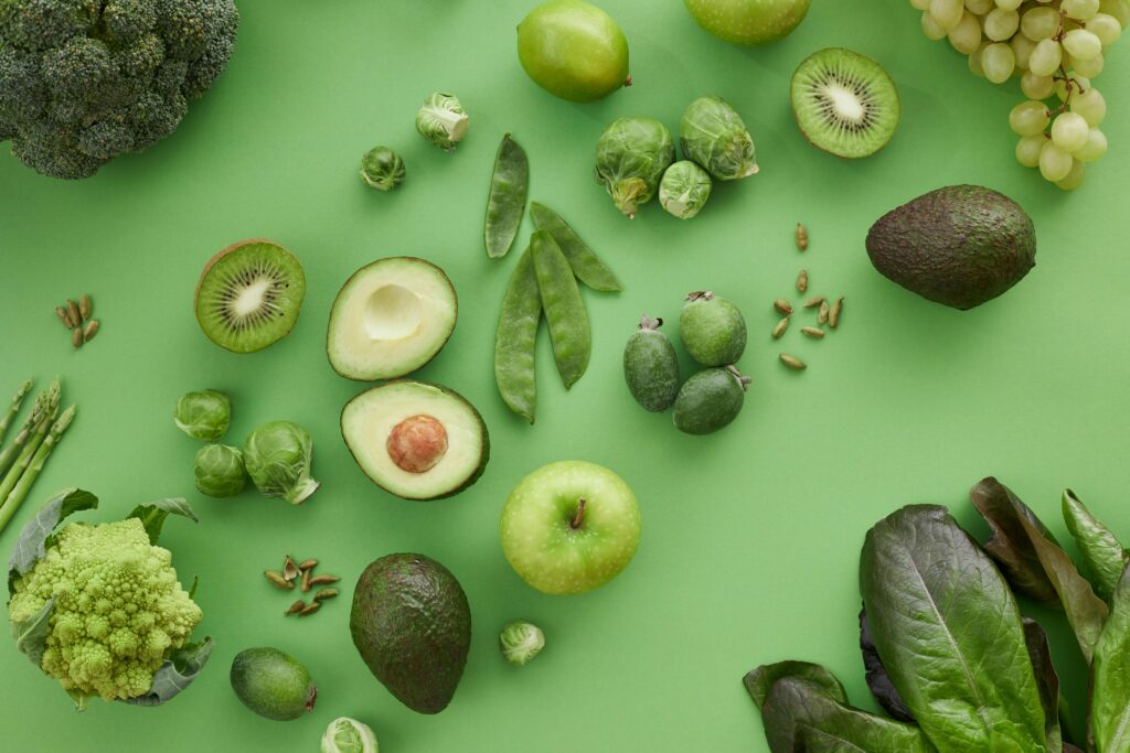 A variety of fresh green fruits and vegetables on a matching background, showcasing healthy organic produce.