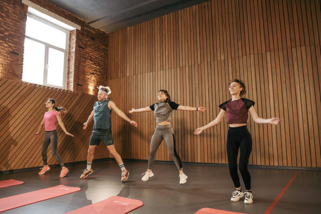 Group of adults doing jumping jacks in modern gym interior.