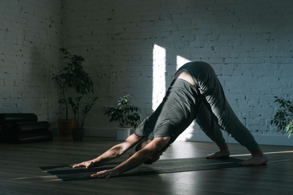 Adult man practicing yoga in downward dog pose on a mat indoors, emphasizing mindfulness and tranquility.