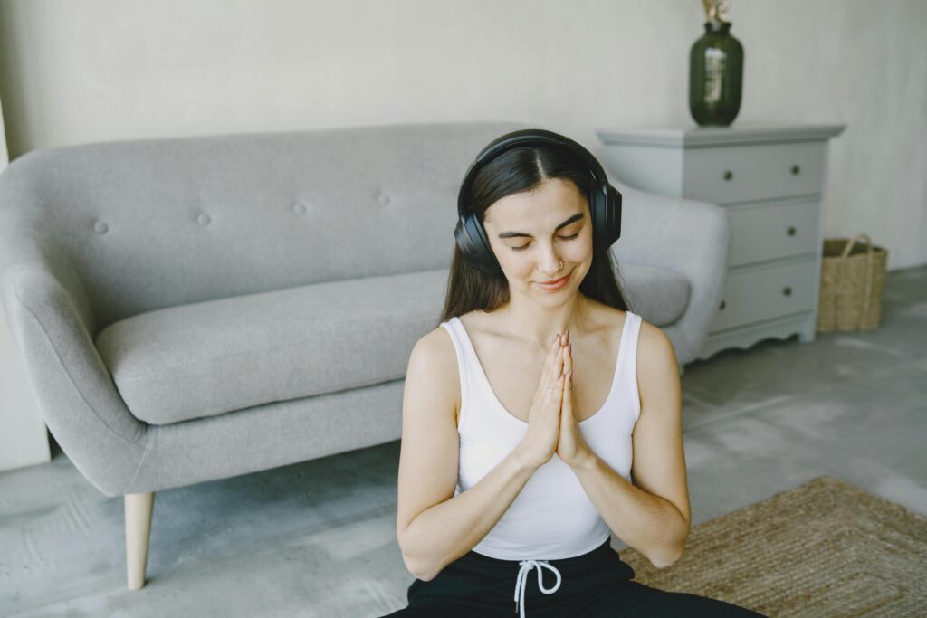 Young woman enjoying meditation with headphones at home, eyes closed, in a peaceful living room setting.