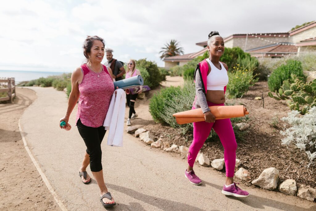 Women walking outdoors with yoga mats, enjoying a morning fitness session.