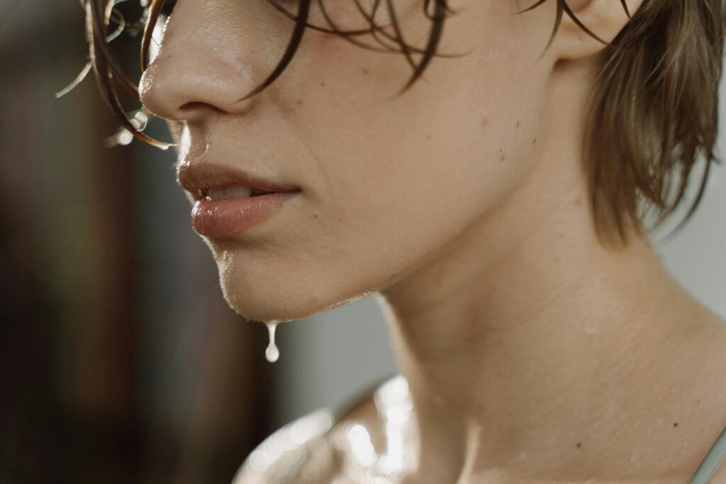 Artistic close-up of a woman's wet face and short hair, capturing a refreshing moment.