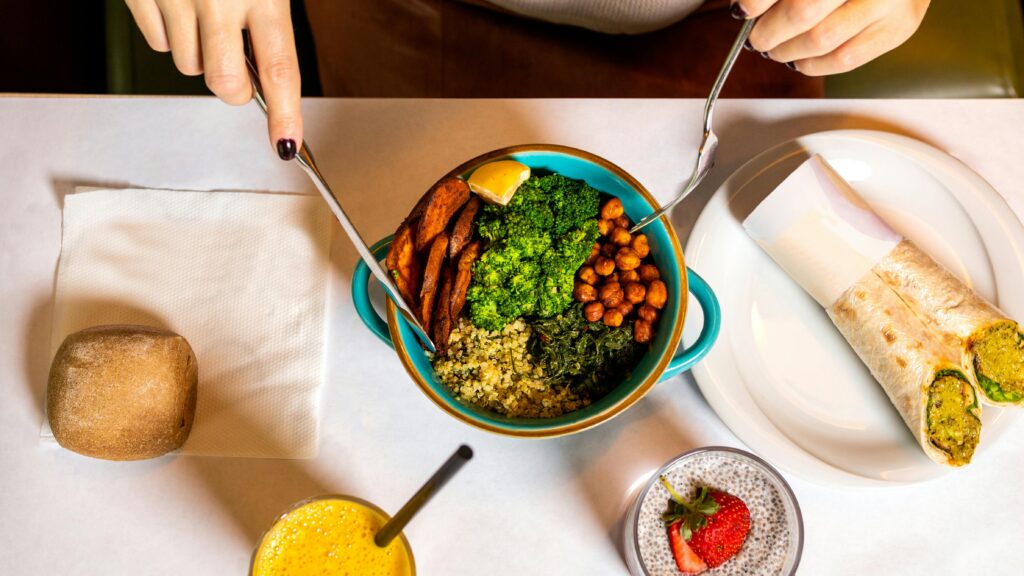 A vibrant vegan meal with fresh ingredients like broccoli, chickpeas, quinoa, served alongside a burrito and refreshing drinks.