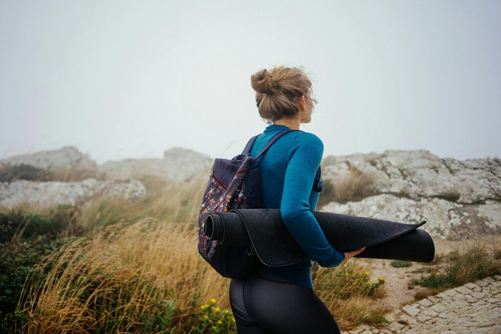 A woman in athletic gear carries a yoga mat through a foggy outdoor landscape, embodying adventure and wellness.