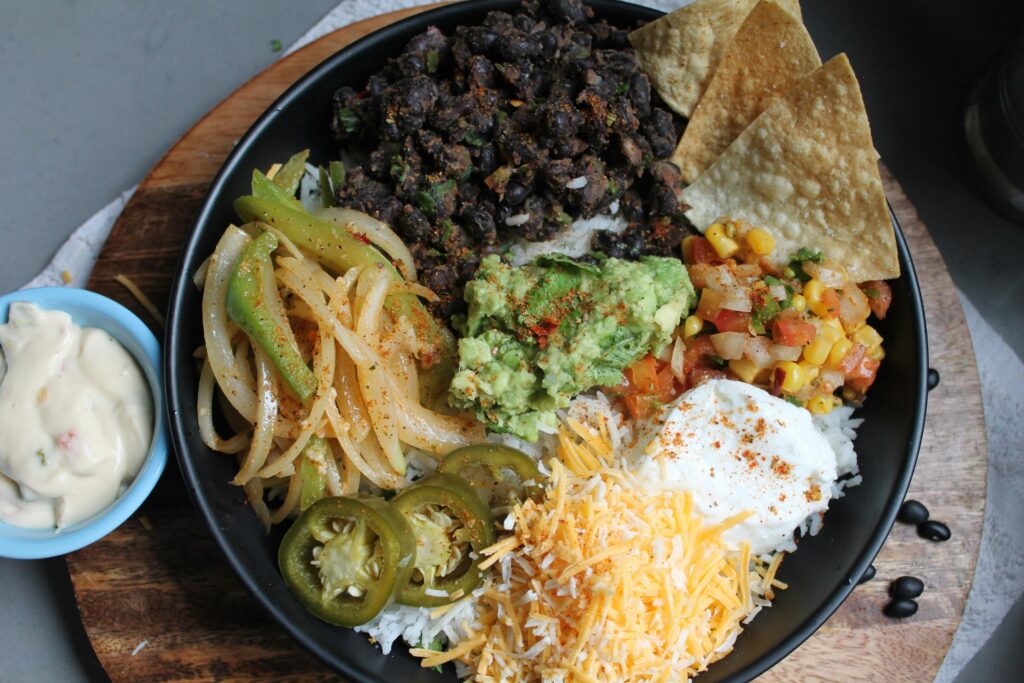 Colorful Mexican burrito bowl featuring guacamole, black beans, and shredded cheese.