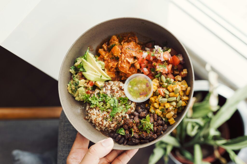 Top view of a vibrant vegan Buddha bowl with quinoa, avocado, and fresh salsa in hand.