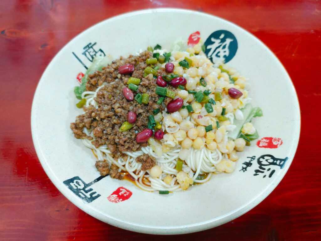 A delicious Chinese noodle dish topped with minced meat, corn, and scallions in a ceramic bowl.