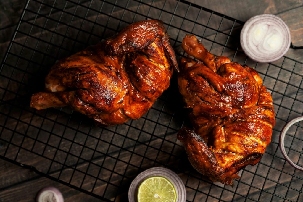 Juicy grilled chicken halves on a cooling rack, garnished with sliced lemon and red onions.